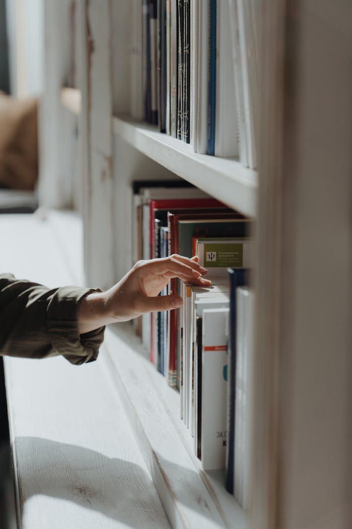 A hand reaches out to select a book from a well-arranged indoor bookshelf.