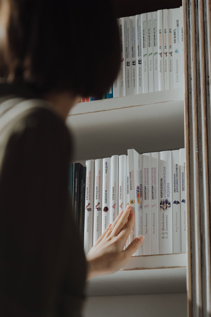 A person examines books on a shelf, capturing a moment of curiosity and learning.